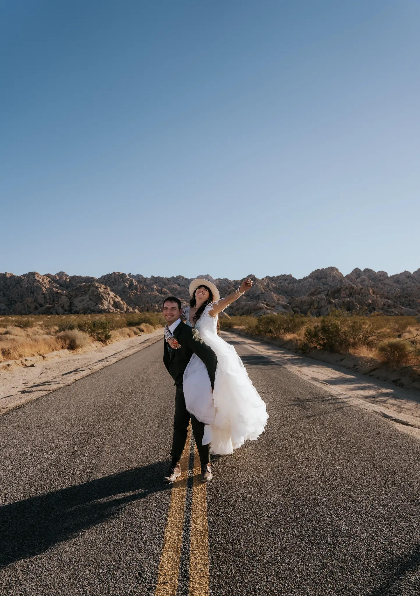 Joyful wedding couple on desert road, Joshua Tree, California